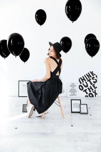 Beyaz arka plan üzerinde siyah poster ve balonlar ile oturan kadın — Stok fotoğraf