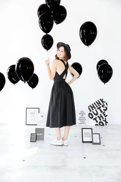 Smiling attractive young woman holding black balloons and looking back — Stock Photo, Image