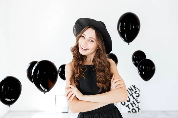 Uśmiechnięta młoda kobieta w czarny kapelusz stojąc z rękami skrzyżowanymi — Zdjęcie stockowe