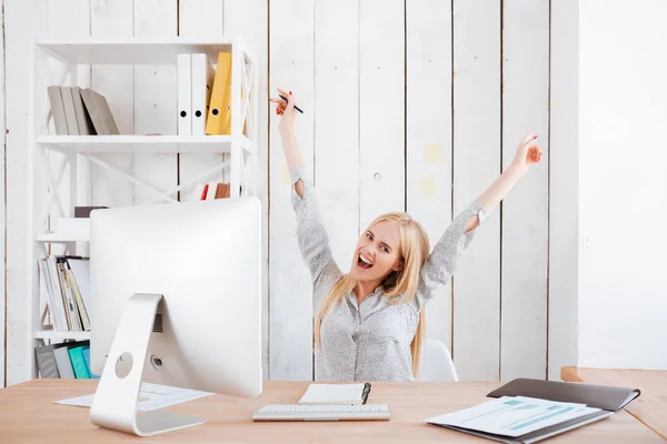 Mulher celebrando o sucesso enquanto está sentada no local de trabalho com as mãos levantadas — Fotografia de Stock