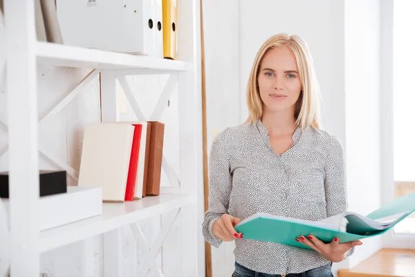 Cheerful businesswoman standing and holding folder at the office — Stock Photo, Image