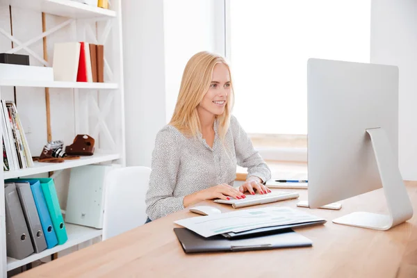 Leende kvinna sitter på hennes arbetsplats och arbeta på dator — Stockfoto