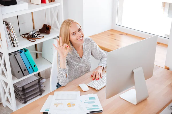 Mujer de negocios mostrando signo aceptable mientras está sentada en su lugar de trabajo — Foto de Stock