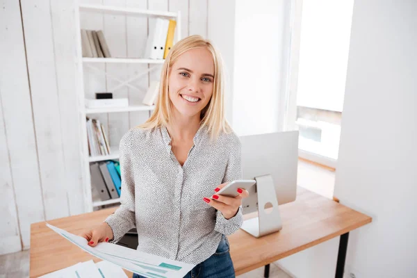 Mujer usando teléfono móvil mientras está de pie en su lugar de trabajo — Foto de Stock