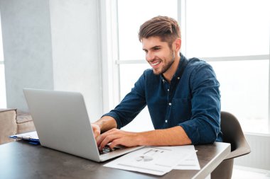 Dizüstü bilgisayar kullanarak ve masada oturan bir genç adam mutlu