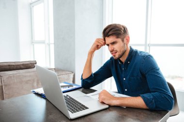 Laptop oturan ve kafa tutan üzgün genç adam