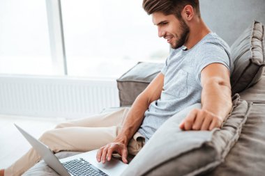 Kanepede oturan ve laptop yanında çalışma neşeli genç adam