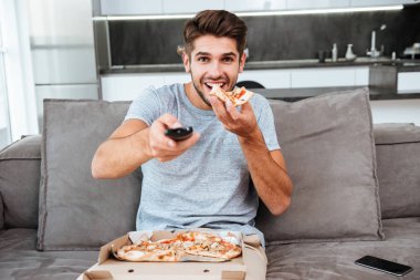 Uzaktan kumanda tutmuş ve düğme pizza yerken adam