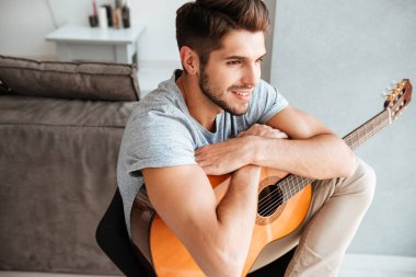 Mutlu adam gitar sandalye ve bir kenara bir görünüm ile oturuyor