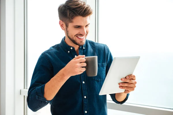 Joven hombre feliz sosteniendo la tableta y beber café — Foto de Stock