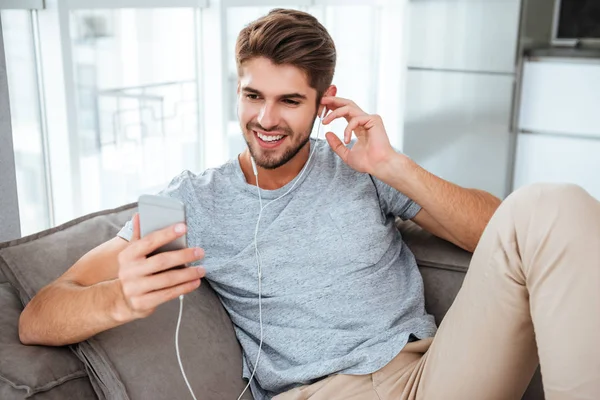 Fülhallgatók embert hallgatni zene rövid idő a kanapén fekszik — Stock Fotó