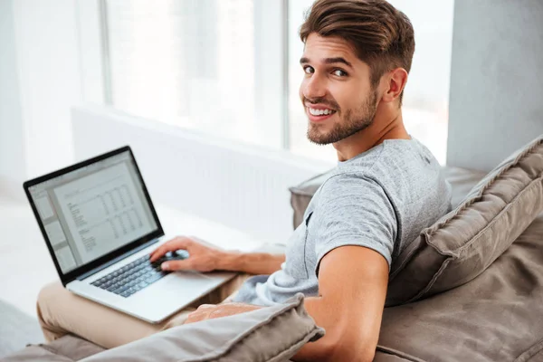 Szczęśliwy młody mężczyzna siedzi z laptopa i patrząc na kamery — Zdjęcie stockowe