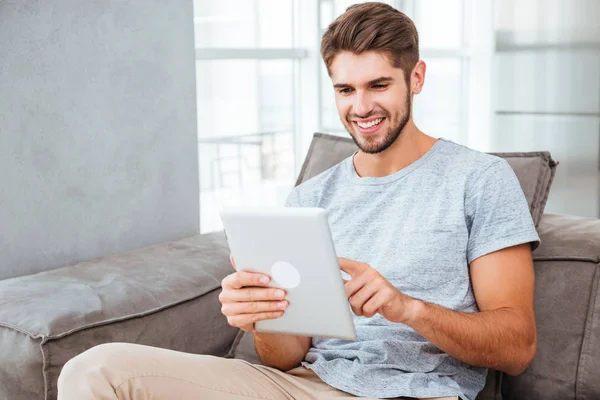 Hombre feliz sentado en el sofá y charlando por la tableta —  Fotos de Stock