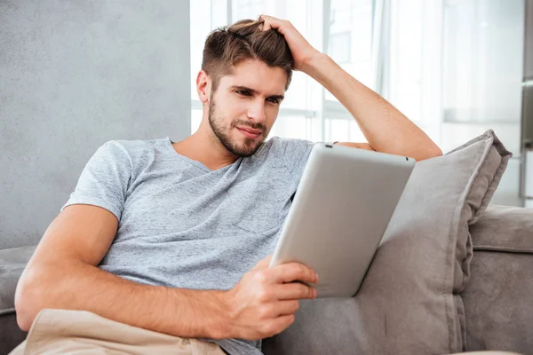Hombre alegre mirando la tableta mientras está sentado en el sofá —  Fotos de Stock