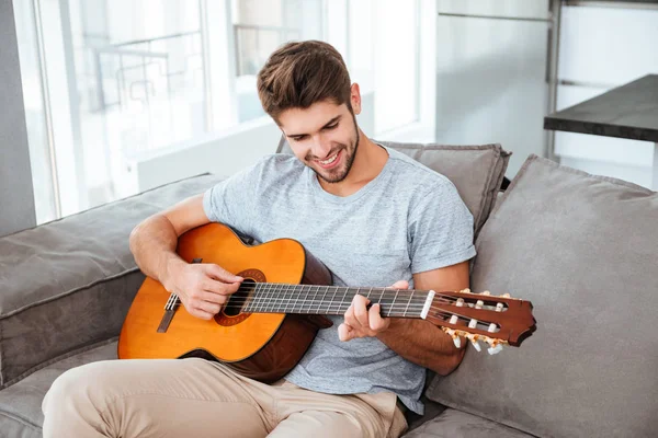 Hombre tocando la guitarra mientras está sentado en el sofá en casa — Foto de Stock