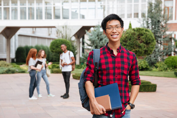 Cheerful asian young man student standing in campus outdoors