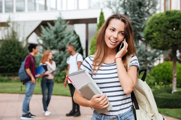 Gelukkige vrouw student permanent en praten op mobiele telefoon buitenshuis — Stockfoto