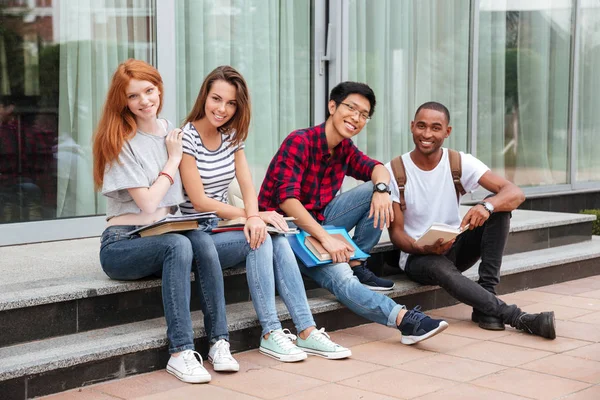 Vrolijke jonge studenten zittend op buiten trappen — Stockfoto