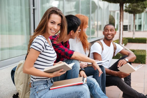 Vrolijke vrouw zitten en lezen boek met haar vrienden outdoors — Stockfoto