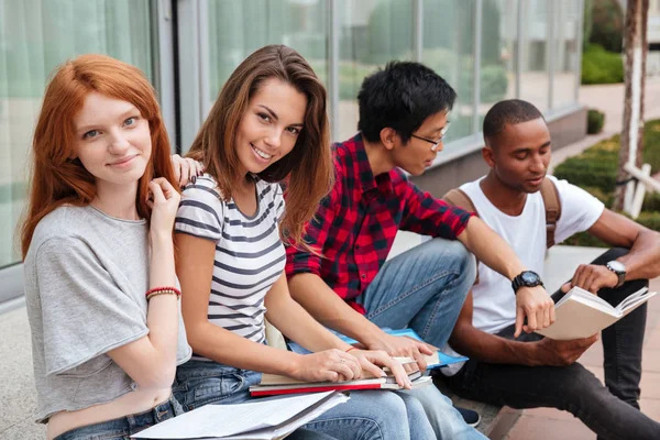 Fröhliche junge Studenten, die draußen sitzen und reden — Stockfoto