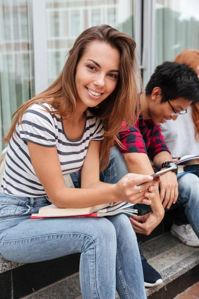 Mulher feliz sentado e usando telefone celular ao ar livre — Fotografia de Stock