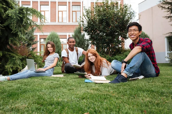 Glimlachende jonge mensen zitten en studeren op gazon buitenshuis — Stockfoto