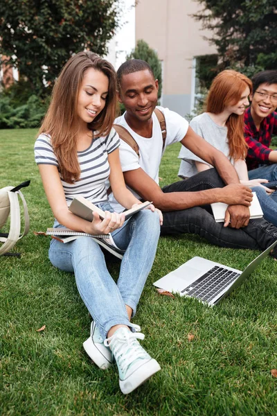 Pessoas felizes lendo livro e usando laptop no gramado ao ar livre — Fotografia de Stock