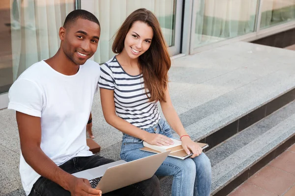 Alegre casal jovem multiétnico sentado e usando laptop ao ar livre — Fotografia de Stock