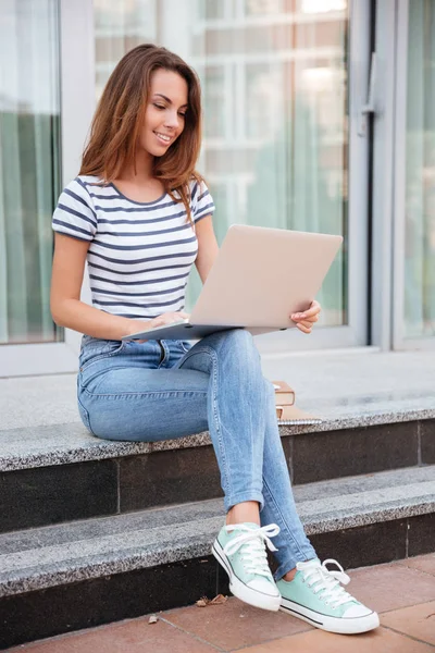 Mujer joven sonriente sentado y trabajando con el ordenador portátil al aire libre —  Fotos de Stock