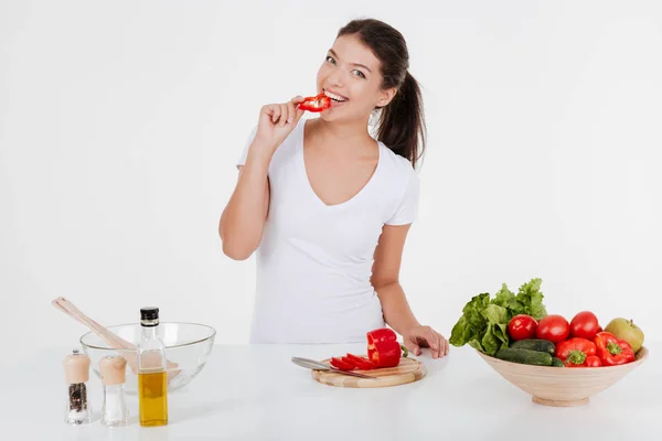 Glückliche junge Frau, die mit Gemüse kocht, während sie es isst — Stockfoto