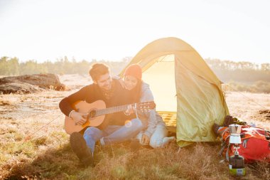 Genç çift gitar yakınlarında kamp çadır ile iyi vakit geçiriyor