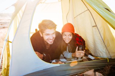 Çadırın içinde yalan ve tablet bilgisayar kullanarak gülümseyen Çift