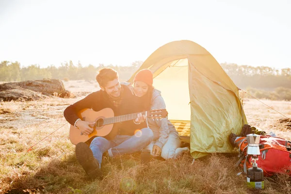 Young couple having good time with guitar near camping tent
