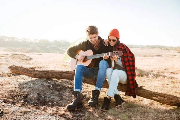 Par ha kul utomhus med gitarr medan du sitter på campingplats — Stockfoto