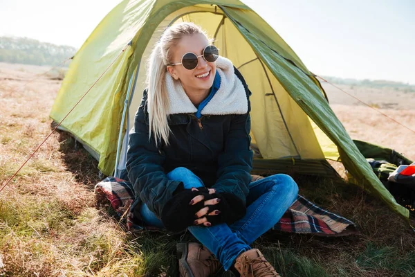 Mujer con gafas de sol y botas sentada cerca de la tienda en el camping —  Fotos de Stock