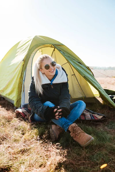 Vrouw in zonnebrillen en laarzen zittend in de buurt van tent op Camping — Stockfoto