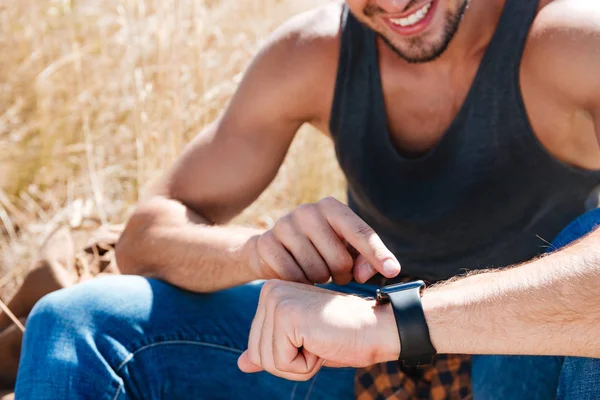 Usmívající se muž pomocí chytré hodinky při posezení venku — Stock fotografie