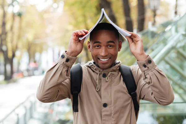Jovem homem africano alegre com caderno na cabeça ao ar livre — Fotografia de Stock