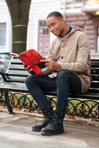 Africano homem feliz lendo um livro enquanto sentado no banco — Fotografia de Stock