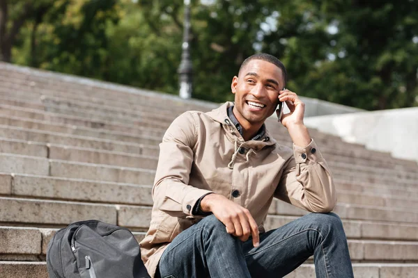 Africano alegre homem sentado na escada enquanto conversa por telefone — Fotografia de Stock