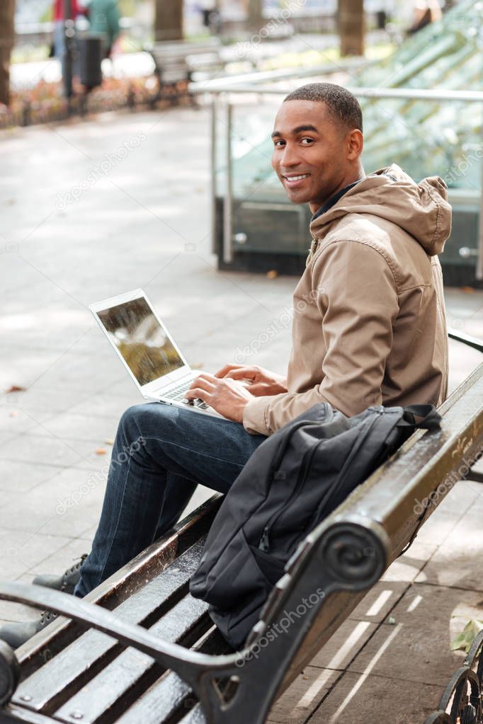 African cheerful man with laptop sitting on a wooden bench