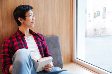 Öğrenci koltukta oturan Üniversitesi kitaplığındaki kitap okumak