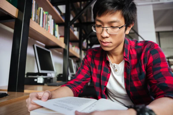 Счастливый азиатский студент читает книгу в библиотеке — стоковое фото