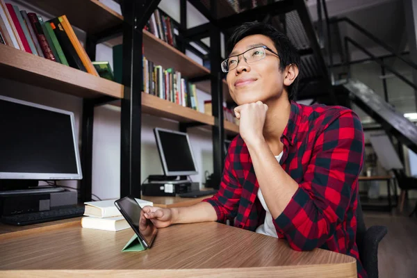 Dreaming asian male using tablet at the library — Stock Photo, Image