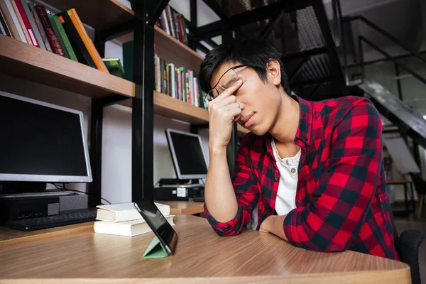 累了亚洲的男学生在图书馆使用平板电脑 — 图库照片