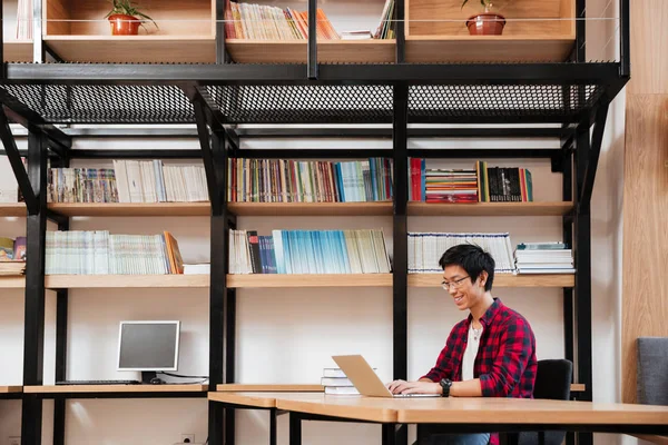 Cheerful asian male using laptop at the library — Stock Photo, Image