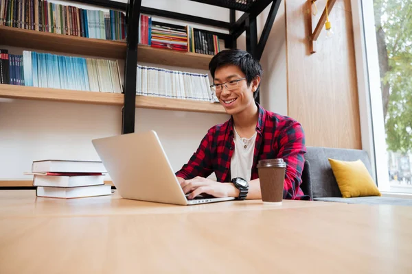 Hombre alegre usando el ordenador portátil en la biblioteca y beber café —  Fotos de Stock