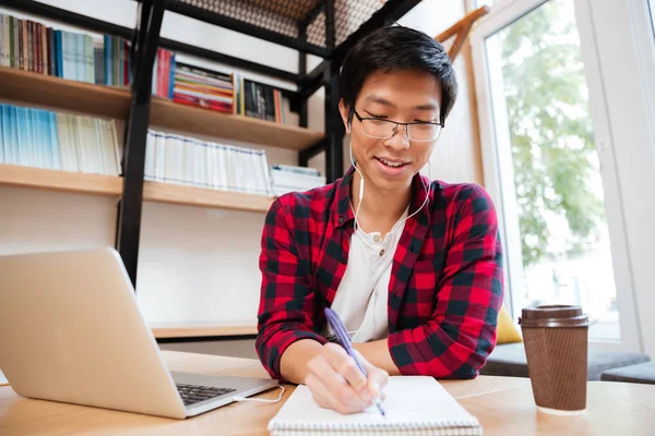 Maschio ascoltare musica durante la scrittura su notebook — Foto Stock