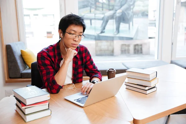 Hombre concentrado usando portátil en la biblioteca y escuchar música —  Fotos de Stock