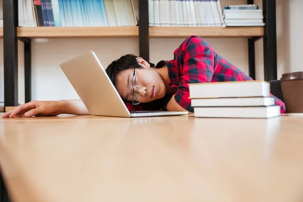Азиатский мужчина спит в библиотеке возле ноутбука и книг — стоковое фото